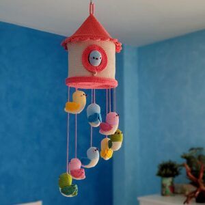 Móvil amigurumi casa de pájaros tejido a crochet, con casita en tonos albaricoque y blanco y ocho pajaritos de colores colgando – patrón Amigudolls en PDF
